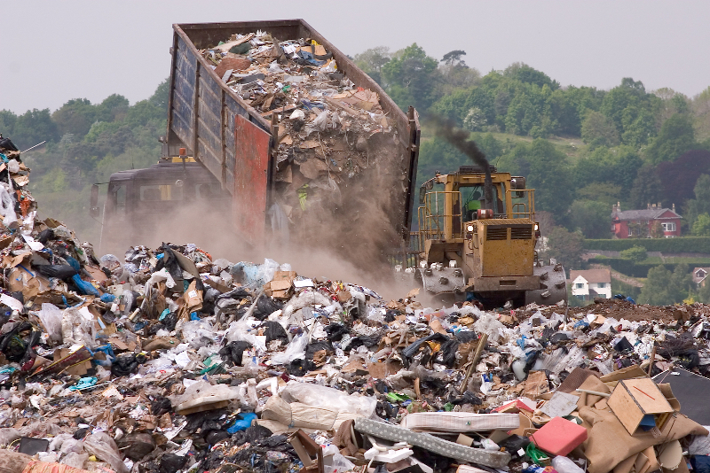 A bulldozer moving garbage on a landfill waste site as a garbage truck dumps more